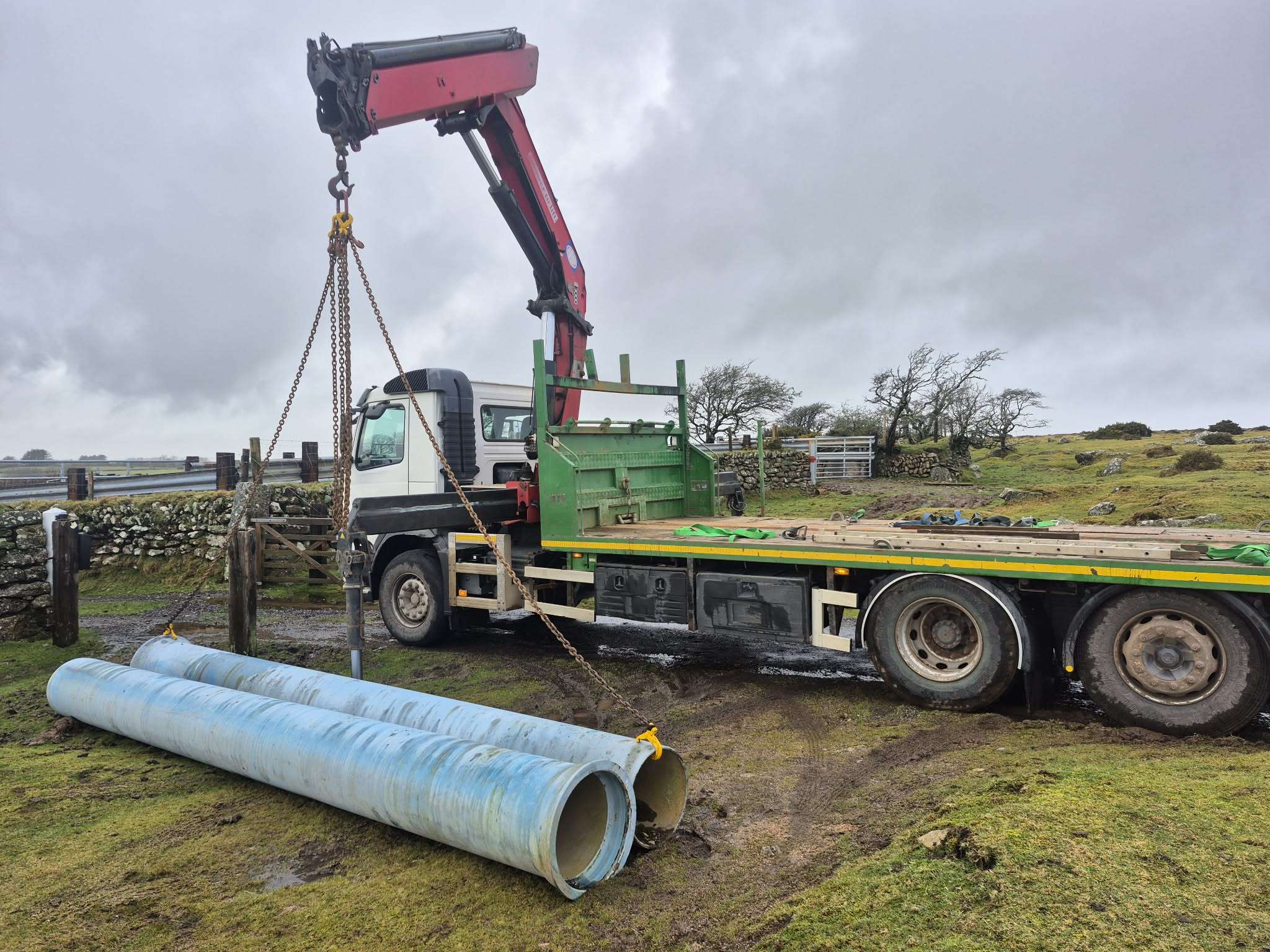 Steel pipe sections lifted by chain on open moorland