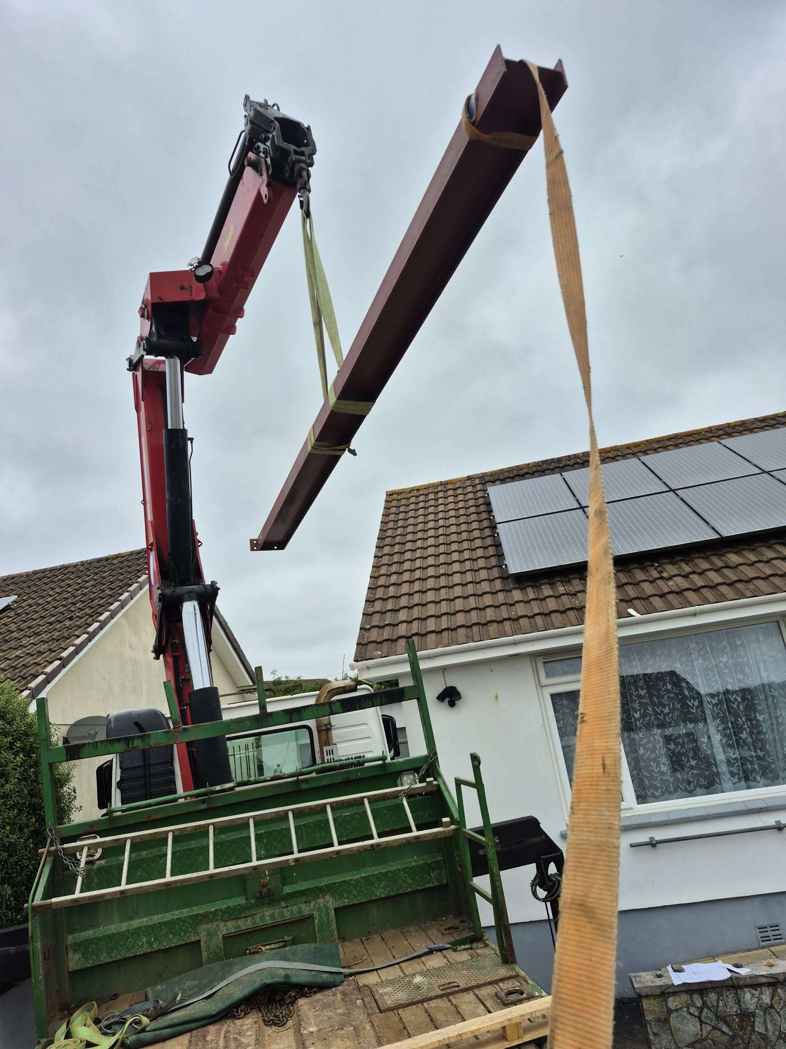 A steel beam lifted by crane over the roof of a bungalow